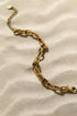 Gold chain bracelet with alternating gold and leopard print links on a sandy background.
