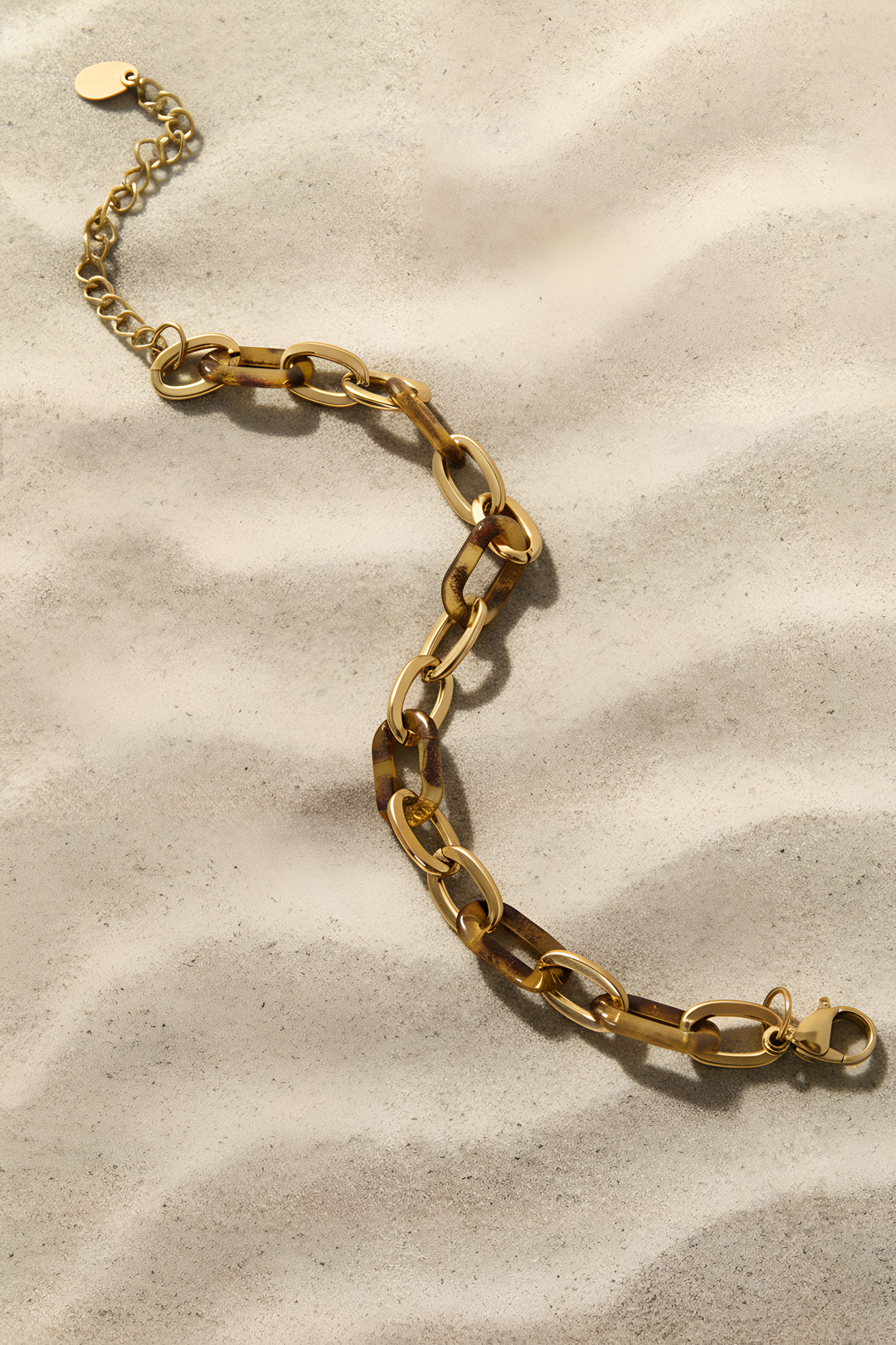 Gold chain bracelet with alternating gold and leopard print links on a sandy background.
