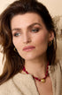 Gold heart hoop earrings on a woman wearing a beige textured jacket and a red necklace.
