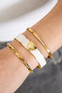 Three gold bangles on a wrist: one with a white band and gold heart, one with small diamonds, and one textured.