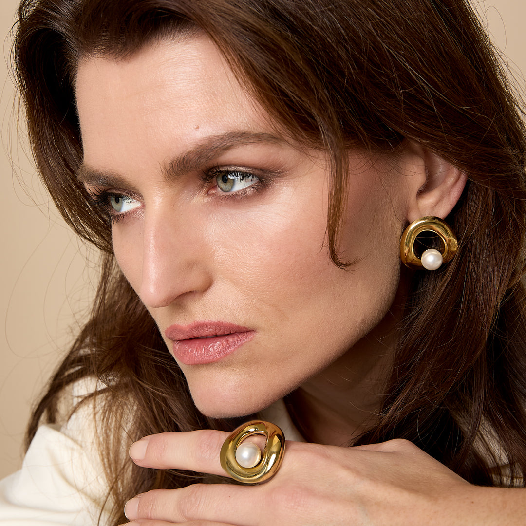 Gold statement ring with a pearl accent on a woman's hand.