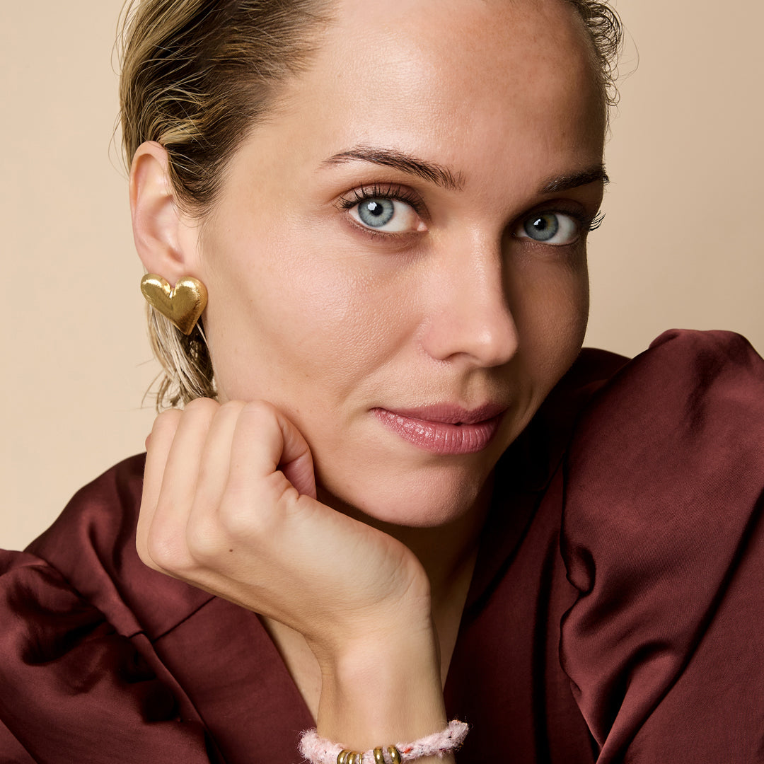 A woman wears a coffee brown/pink rope bracelet with a gold heart charm and gold rings.