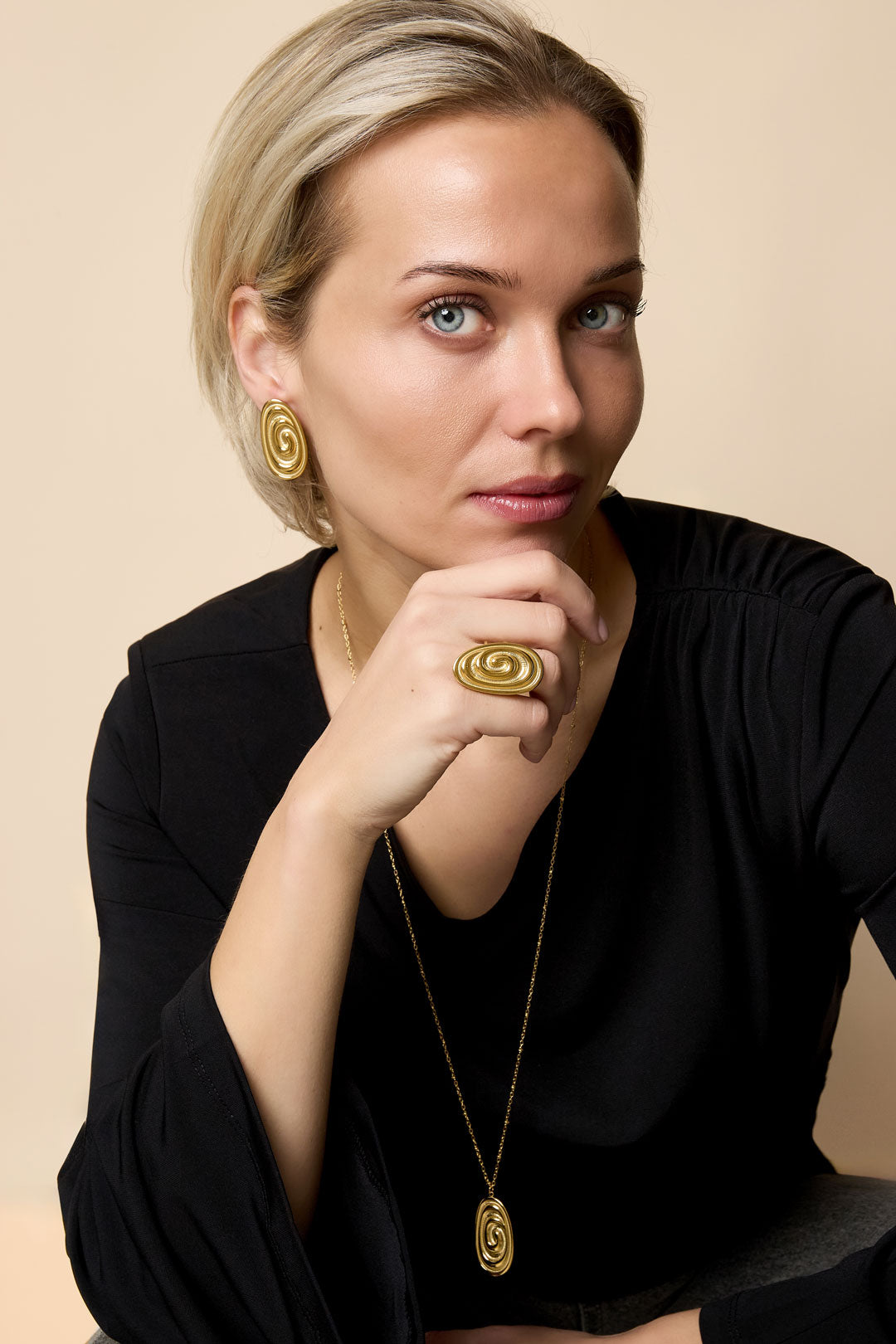 Gold irregular spiral ring on a woman's finger, with matching earrings and necklace.