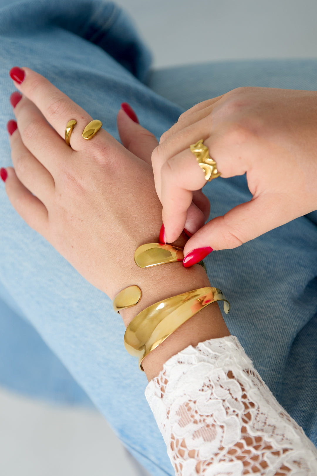 Gold irregular cuff bracelet on a woman's wrist, paired with a matching ring.
