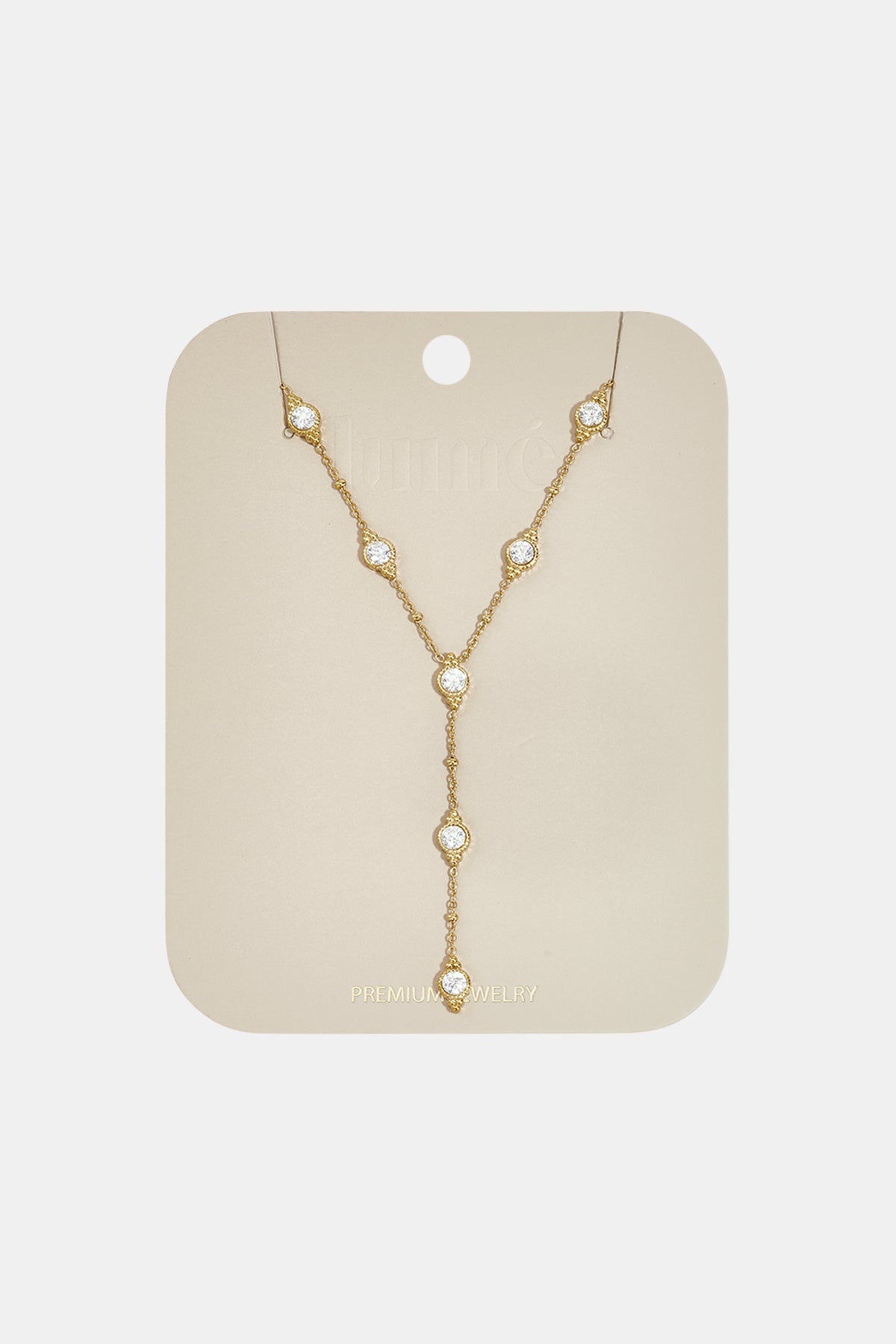 Gold necklace with five clear stones arranged in a Y-shape on a beige card.