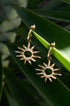 Gold sun drop earrings with pointed rays, hanging from a hoop.