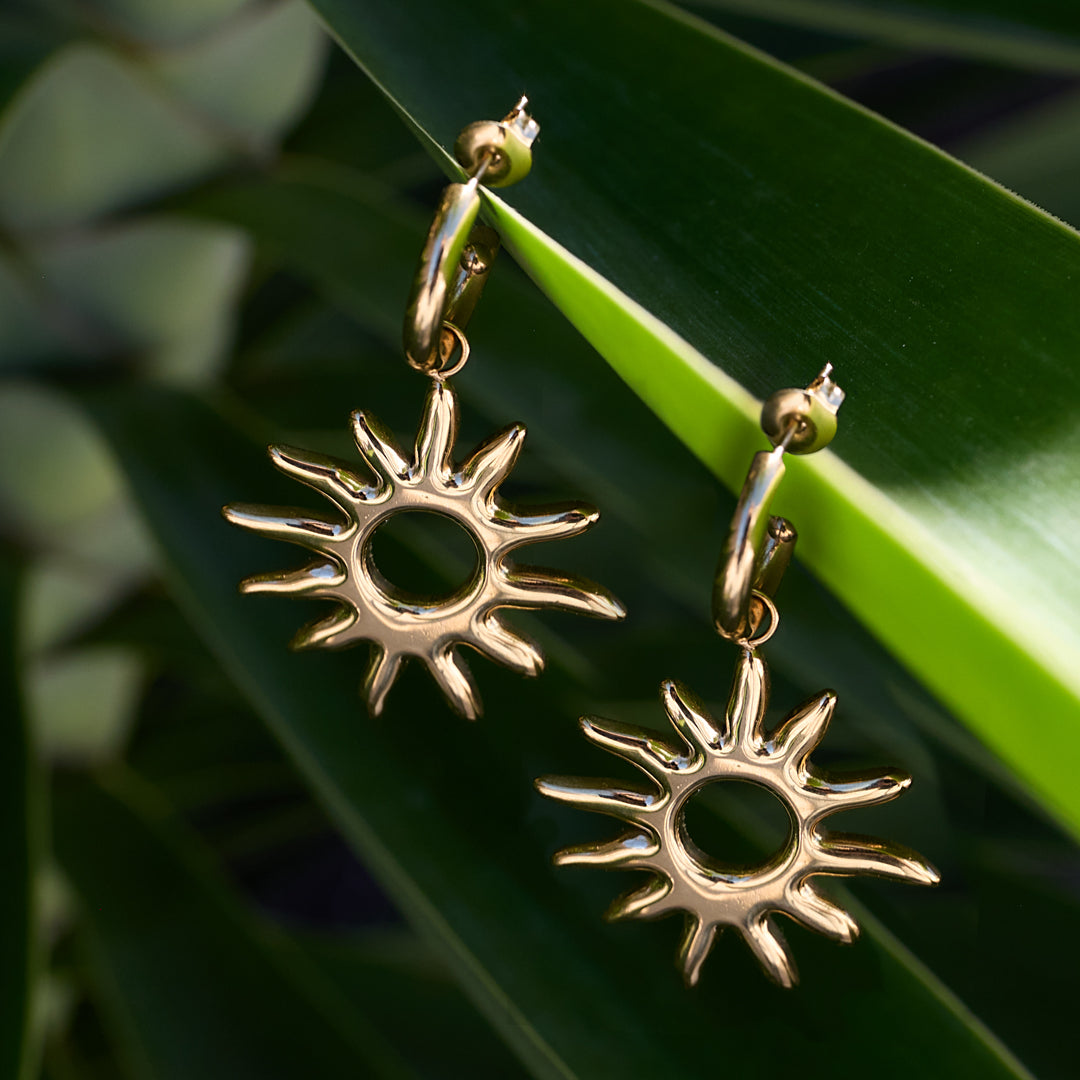 Gold sun drop earrings with pointed rays, hanging from a hoop.