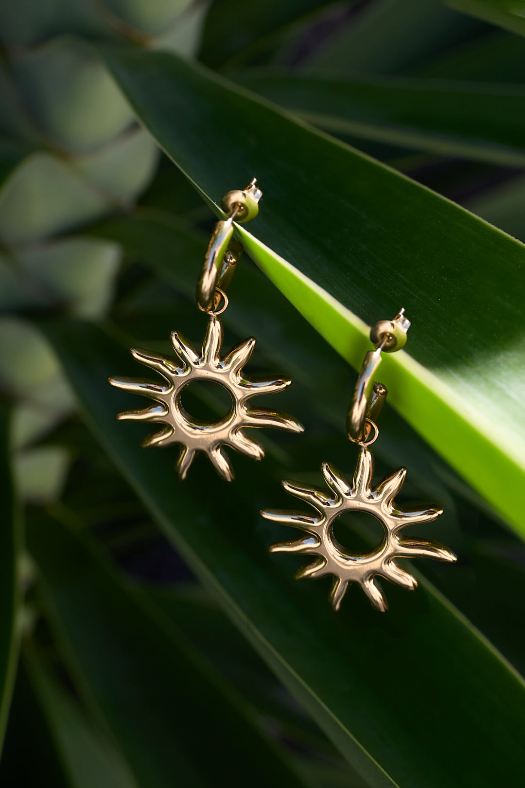 Gold sun drop earrings with pointed rays, hanging from a hoop.