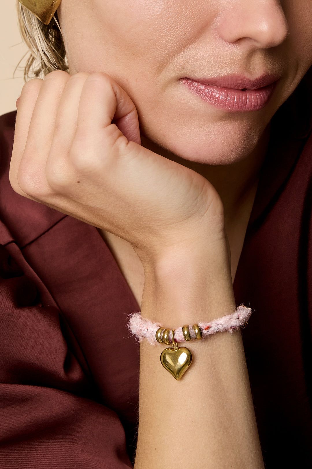 Pink rope bracelet with gold heart charm and gold rings.