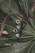 Gold drop earrings with textured rings and pave zircon heart charms on a green leaf.