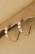 Gold hoop earrings with three clear stones each, set against a brown background.