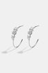 Silver hoop earrings with three clear stones each, casting shadows on a white background.