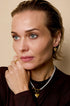 Gold heart drop earrings on a woman with a pearl necklace and gold ring.
