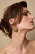 Gold sun drop earrings on a woman's ear, with a gold bow hair clip in her hair.
